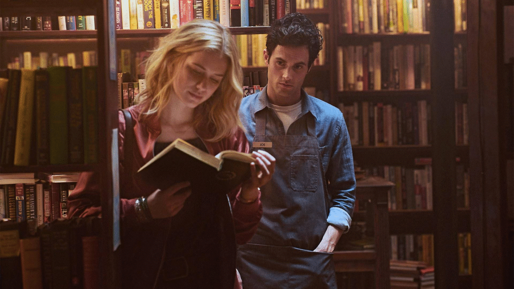 Joe Goldberg observa Beck lendo um livro em cena da série You da Netflix, ambientada em uma livraria